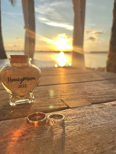 two wedding rings sitting on top of a wooden table next to a bottle with the sun setting in the background