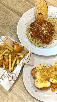 two white plates topped with pasta and french fries next to bread on a table top