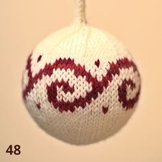 a knitted ornament hanging from a string on a white wall with red and white designs