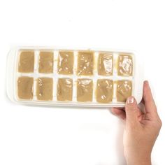 a hand holding an ice cube tray filled with peanut butter