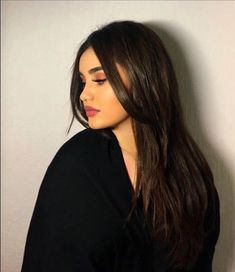 a woman with long hair standing against a wall and looking off to the side, wearing a black shirt