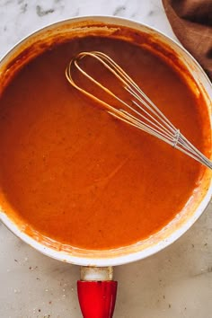 a bowl filled with sauce and whisk sitting on top of a white counter