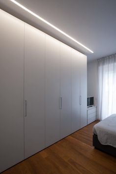 a bedroom with white closets and wooden flooring next to a bed in front of a window