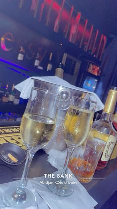 two wine glasses sitting on top of a table next to bottles of alcohol and liquor