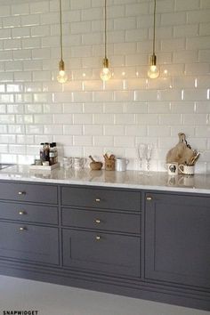 a kitchen with gray cabinets and white subway backsplash, gold hardware on the counter