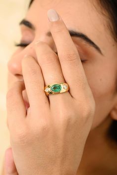 a woman holding her hand up to her face with a green stone in the middle