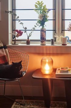 a black cat sitting on a chair next to a table with a book and vase