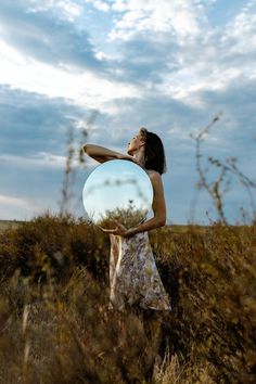 a woman holding a frisbee while standing in tall grass on a cloudy day