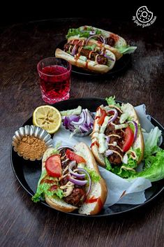 two sandwiches with meat, lettuce, tomatoes and onions on a black plate