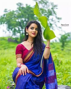 a woman in a blue sari holding a green leaf