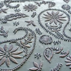 an embroidered table cloth with flowers and leaves on it's side, in grey