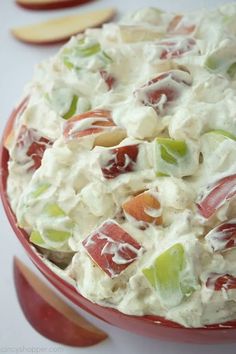 a red bowl filled with fruit salad on top of a white table next to sliced apples