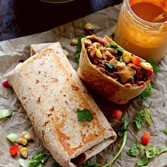 two burritos sitting on top of a piece of paper next to a jar of sauce