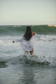 a woman in white shirt walking into the ocean