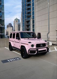 a pink mercedes benz g63 is parked in a parking lot next to tall buildings