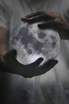 two hands holding a glowing blue ball in the dark night sky with full moon behind them