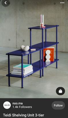 a blue shelf sitting on top of a white floor next to a vase and books