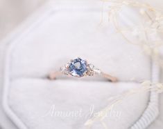 an engagement ring with a blue topaz surrounded by white flowers and branches in the background