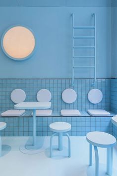 a blue tiled bathroom with white tables and stools next to a round light fixture