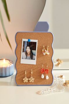 a photo frame with earrings on it next to a candle and bead necklaces