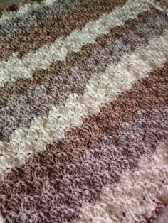 a crocheted blanket is laying on top of a bed with the colors of brown, white and tan