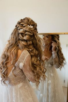 a woman in a wedding dress looking at herself in the mirror with her hair pulled back