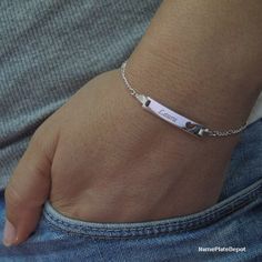 a person wearing a silver bracelet with a name tag on it's side and two hearts in the middle