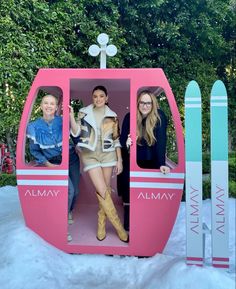 three people in a pink ski lift with snowboards on the ground and trees behind them