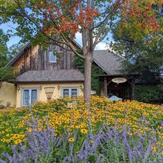 a house in the middle of a field with wildflowers and trees around it