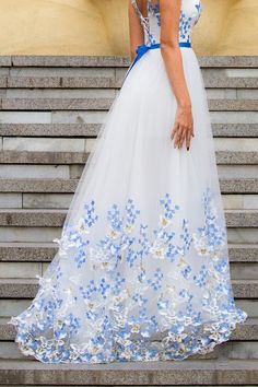 a woman in a blue and white dress is standing on some steps with her hands behind her back