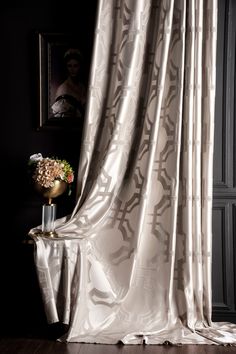 a vase with flowers sitting on top of a table next to a curtain