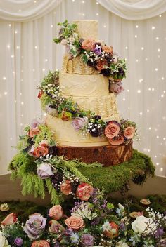 a three tiered cake with flowers and greenery on the top is surrounded by moss