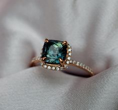 a fancy ring with an emerald colored stone surrounded by white and brown diamonds on a cloth