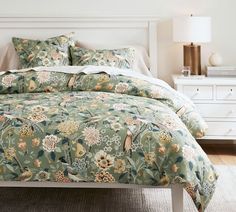 a bed with a green floral comforter and matching pillows in a white bedroom setting