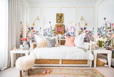 a white bed sitting in a bedroom next to a wall covered in flowers and plants