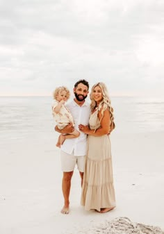 a man, woman and child standing on the beach with their arms around each other