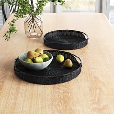 two black trays sitting on top of a wooden table next to a bowl of fruit