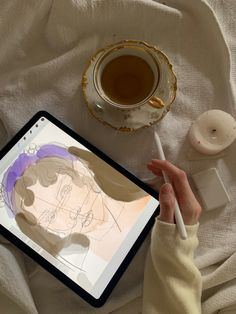 a person drawing on an ipad next to a cup of tea and a saucer