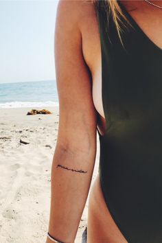 a woman with a tattoo on her arm standing in front of the ocean and sand