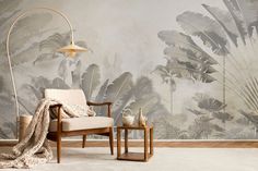 a chair and table in front of a wall with palm leaves on it, next to a lamp