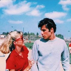 a man and woman standing next to each other on a baseball field with the sky in the background