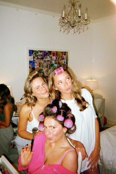 three young women standing next to each other in front of a bed and chandelier