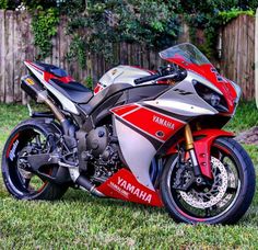 a red and silver motorcycle parked on top of a lush green field next to a wooden fence