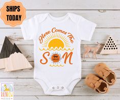 a baby bodysuit with the words here comes me, and an orange sun on it