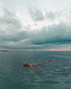 a man swimming in the ocean under a cloudy sky