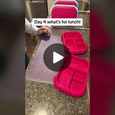 a pink lunch box sitting on top of a counter next to a plastic container filled with food