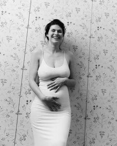 a pregnant woman poses in front of a floral wallpaper