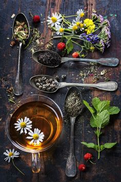 spoons filled with tea and flowers on top of a wooden table next to other items