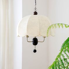 a white lamp hanging from a ceiling next to a green plant