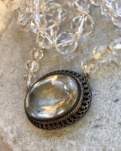 a necklace with an oval pendant surrounded by clear crystal beads and chains on a marble surface